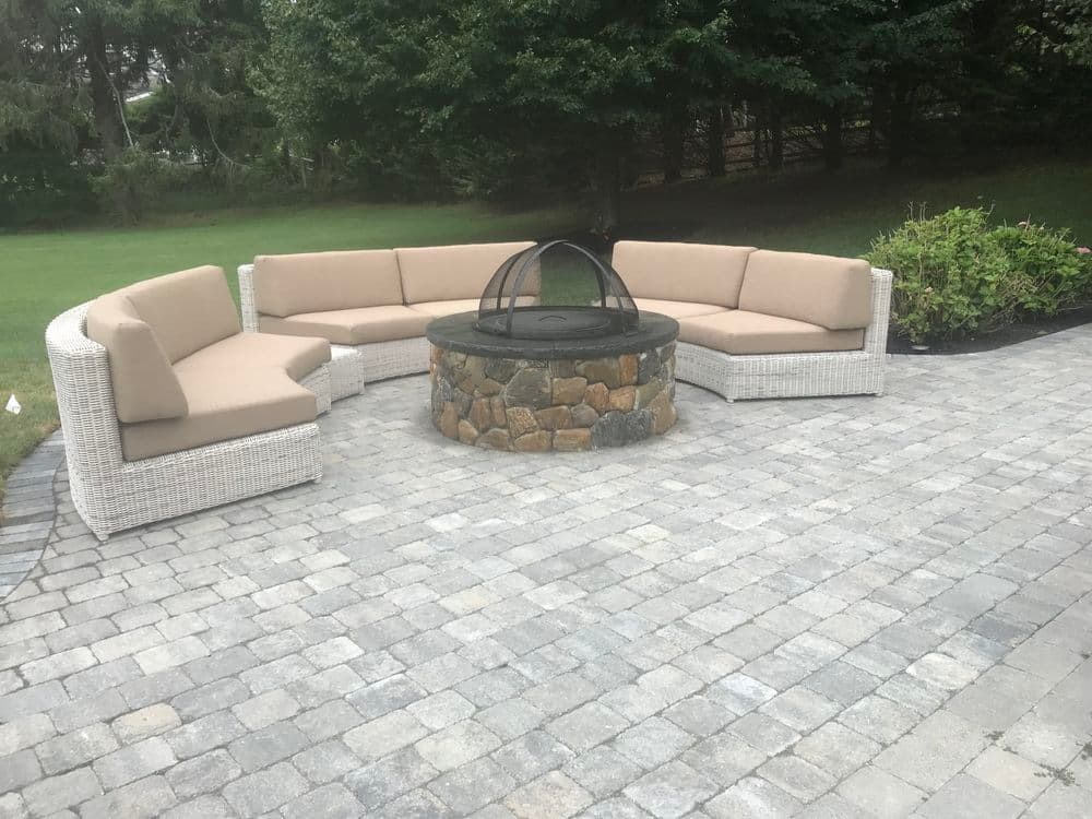 Outdoor fire pit with circular seating area and stone base, surrounded by green landscaping.