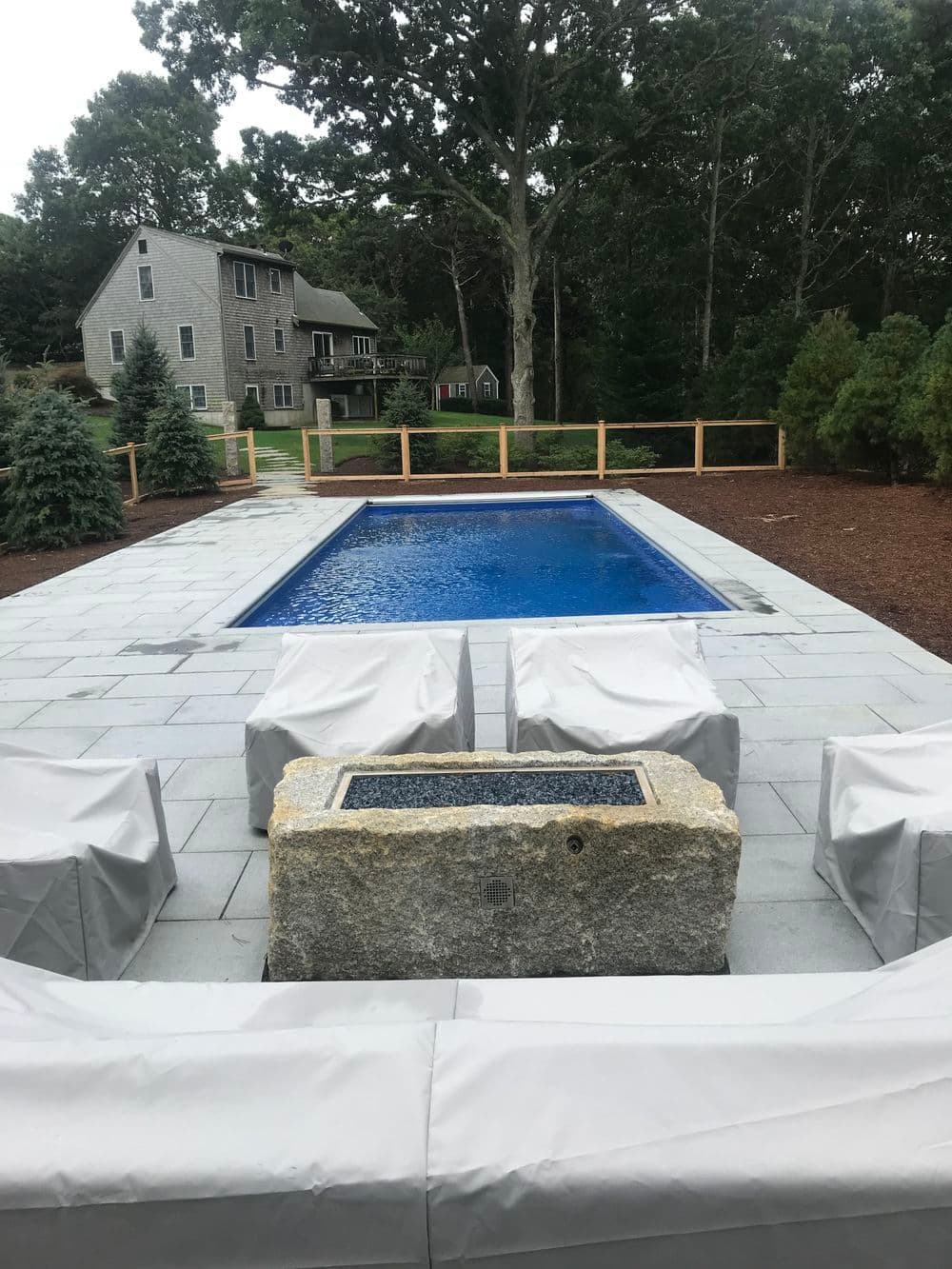 Elegant backyard pool with stone seating and lush greenery in a tranquil setting.