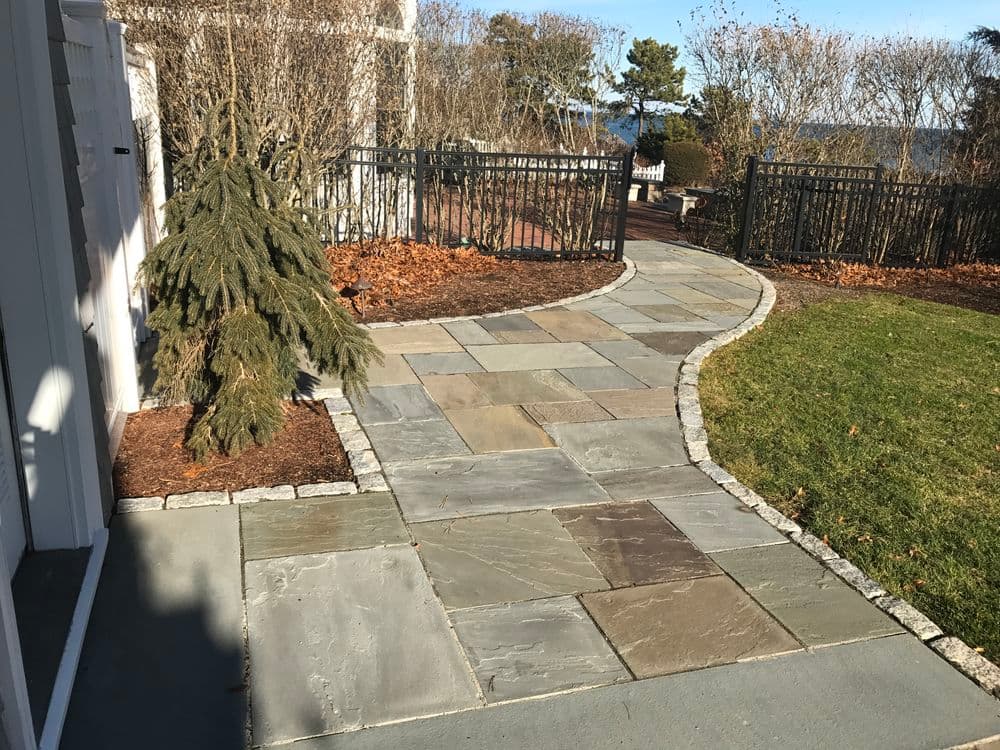 Elegant stone pathway winding through landscaped yard, surrounded by greenery and fencing.