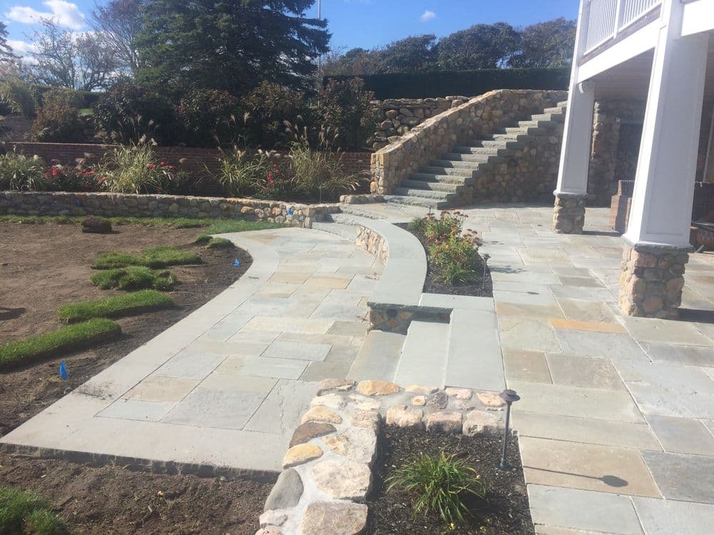 Landscaped garden with stone walkway, stairs, and greenery under a blue sky.