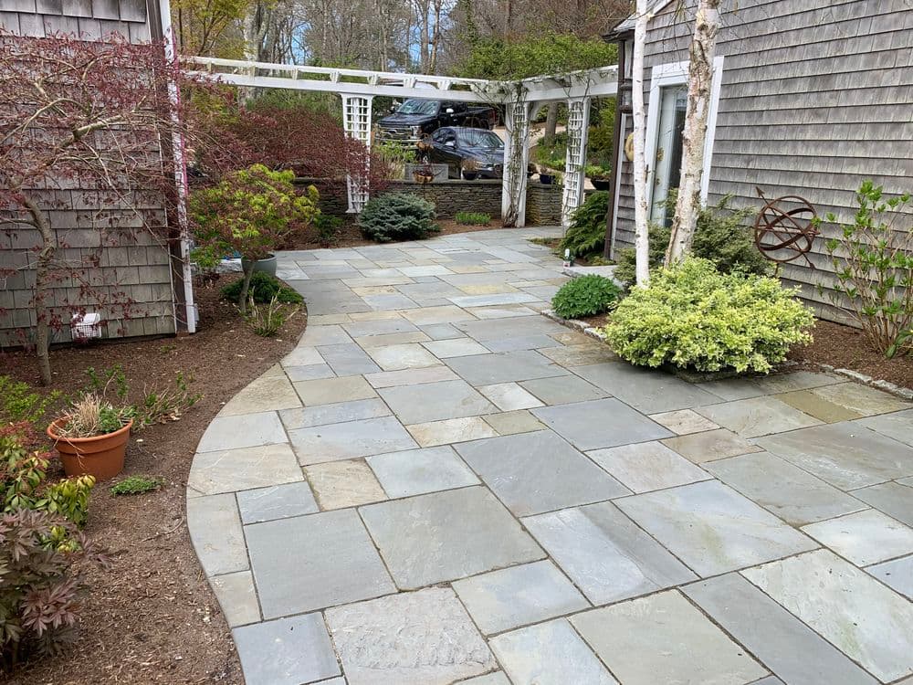 Curved stone pathway surrounded by landscaped greenery and a trellis in a residential garden.