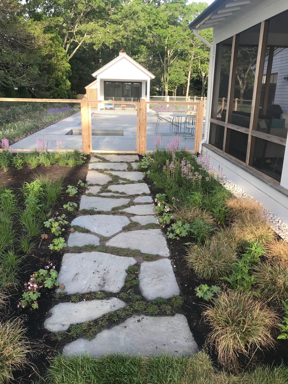 Stone pathway through landscaped garden leading to a modern backyard patio.