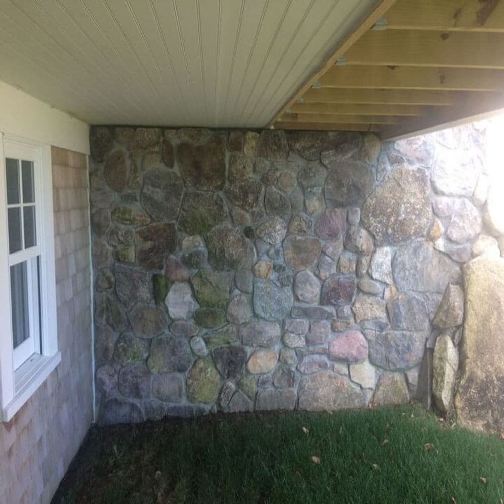 Stone wall under deck with window and grass area, showcasing natural textures and structure.