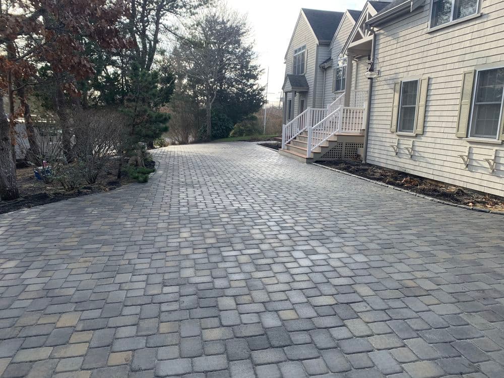 Paved stone driveway leading to a residential home, surrounded by greenery and shrubs.