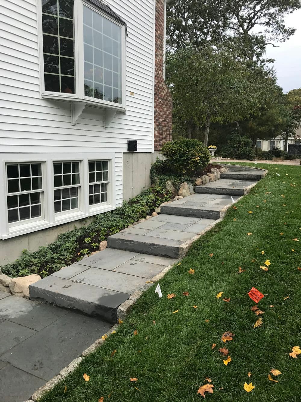 Slate stone pathway leading to a home, bordered by lush green grass and landscaping.