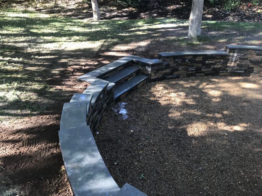 Curved stone seating area with steps in a landscaped yard, perfect for outdoor gatherings.