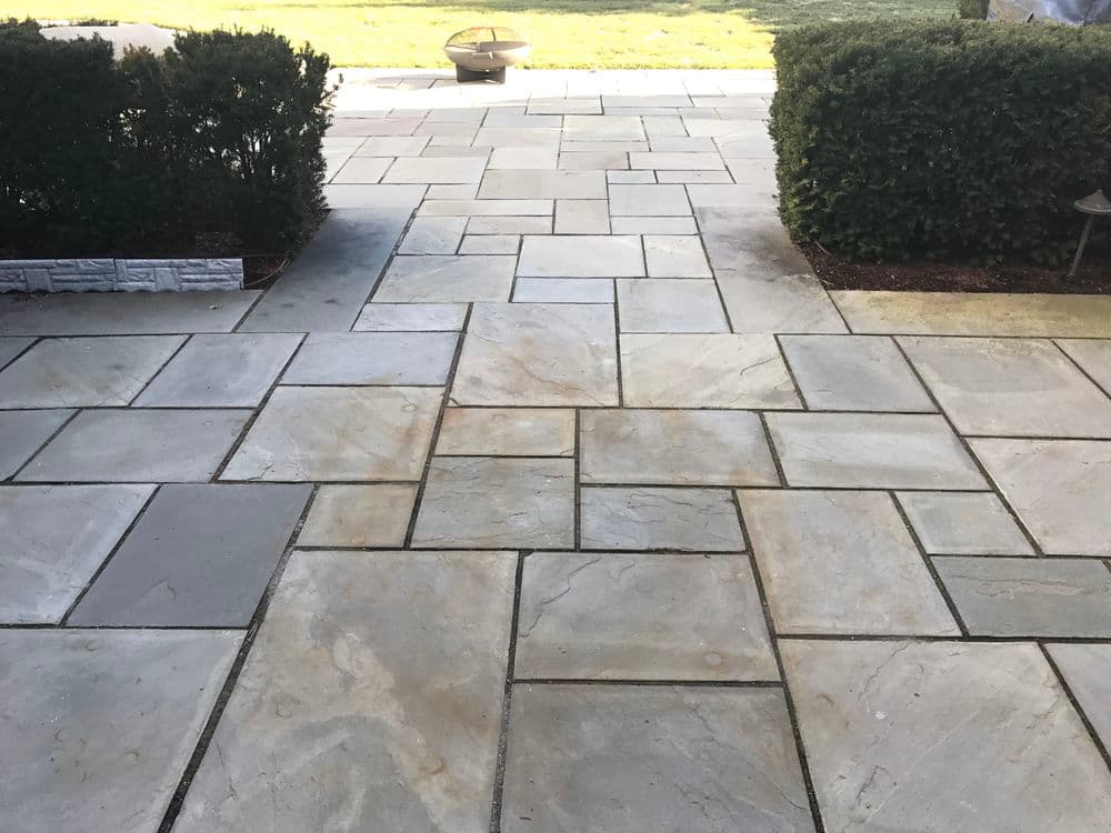 Paved walkway with natural stone tiles, bordered by manicured hedges and a clear sky.