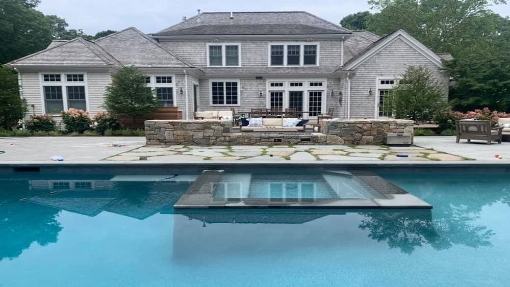 Modern home with stone patio and pool reflecting the serene backyard garden views.