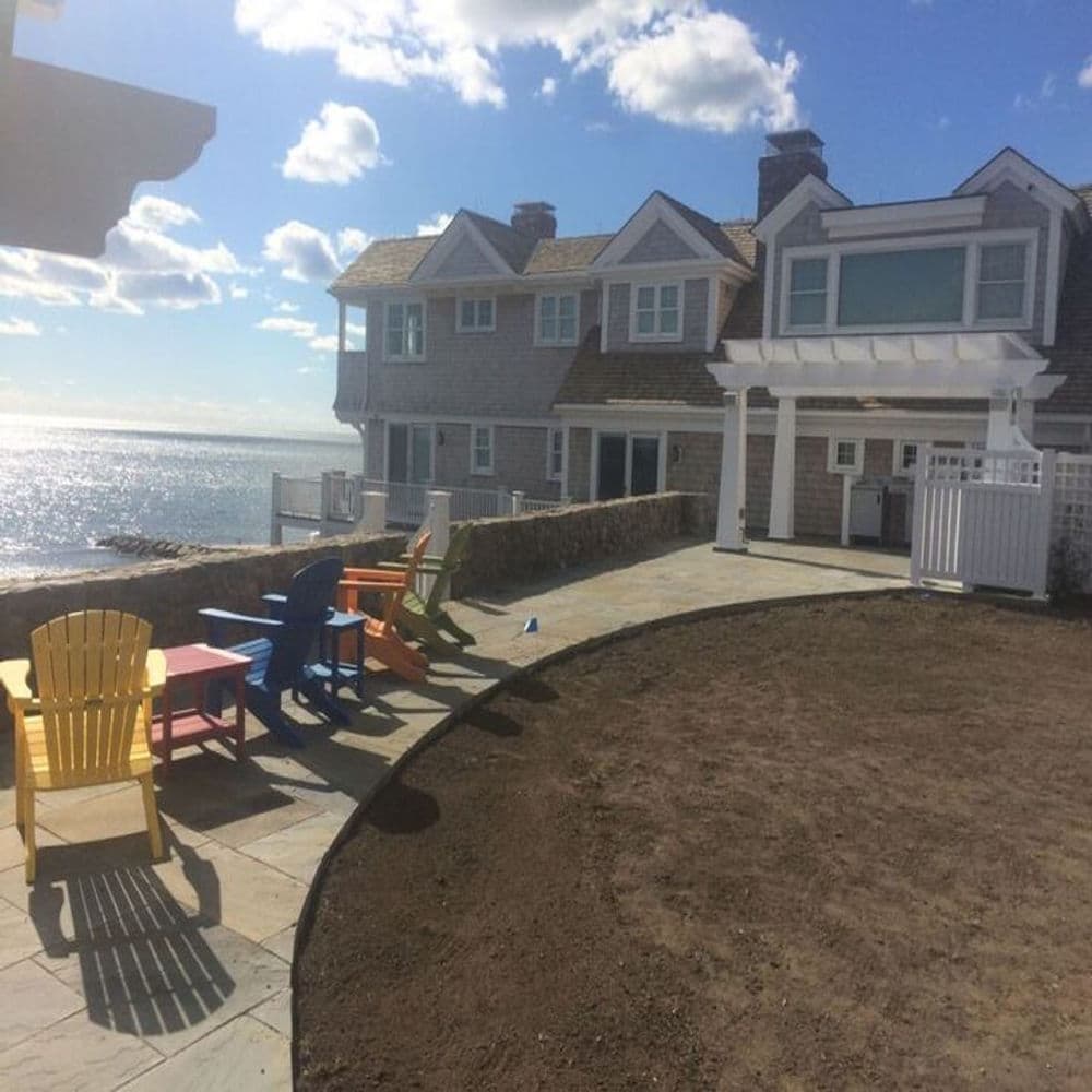 Colorful outdoor chairs by a seaside house with ocean view and blue sky.