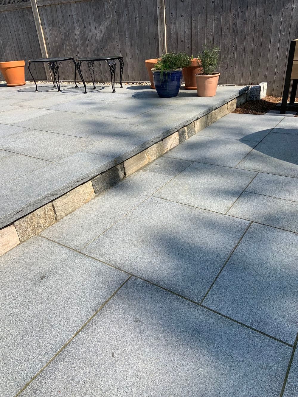 Outdoor stone patio with steps, planters, and garden furniture in a sunny setting.