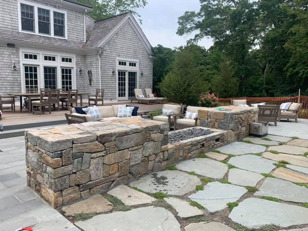 Stone outdoor patio with seating area and fire pit near a modern home and deck.