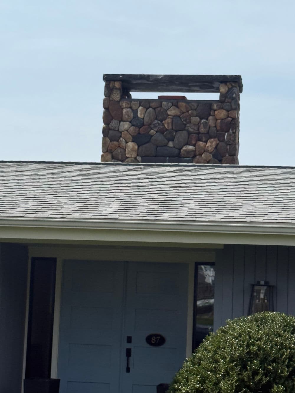 Charming home with a stone chimney on a sloped roof and a blue front door.