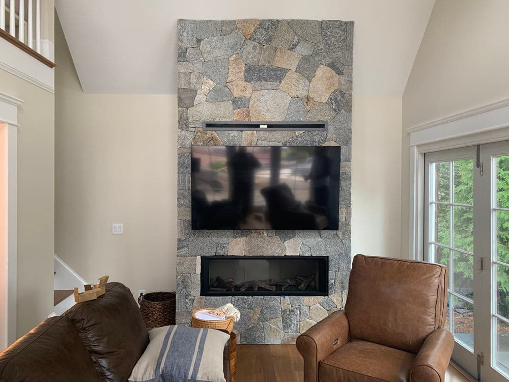 Modern living room with a stone fireplace, mounted TV, and cozy leather armchair.