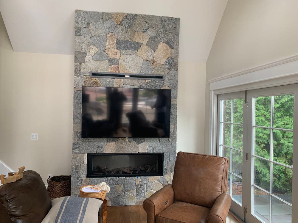 Modern living room with a stone fireplace, mounted TV, and cozy leather armchair.