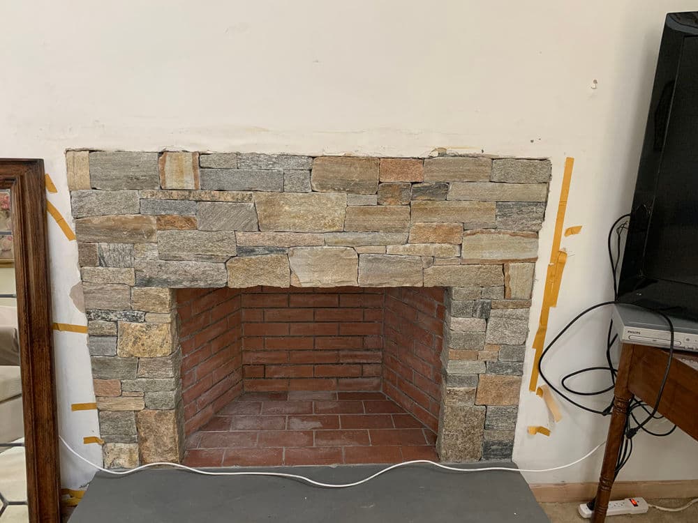 Stone fireplace with brick interior, unpainted wall, and nearby furniture pieces.