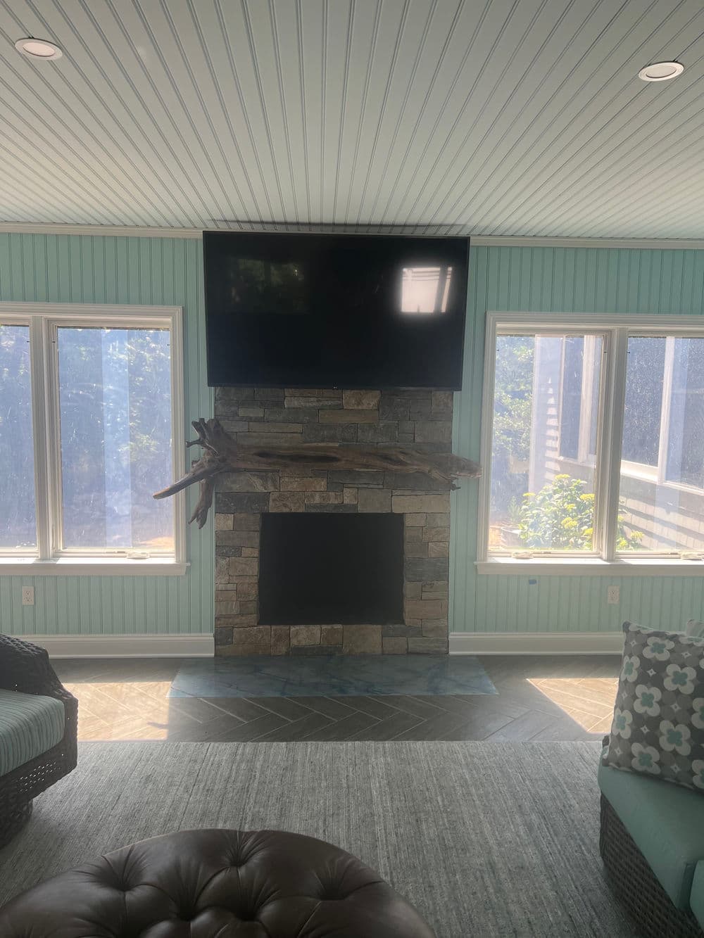 Bright sunroom featuring a stone fireplace, mounted TV, and cozy seating arrangements.
