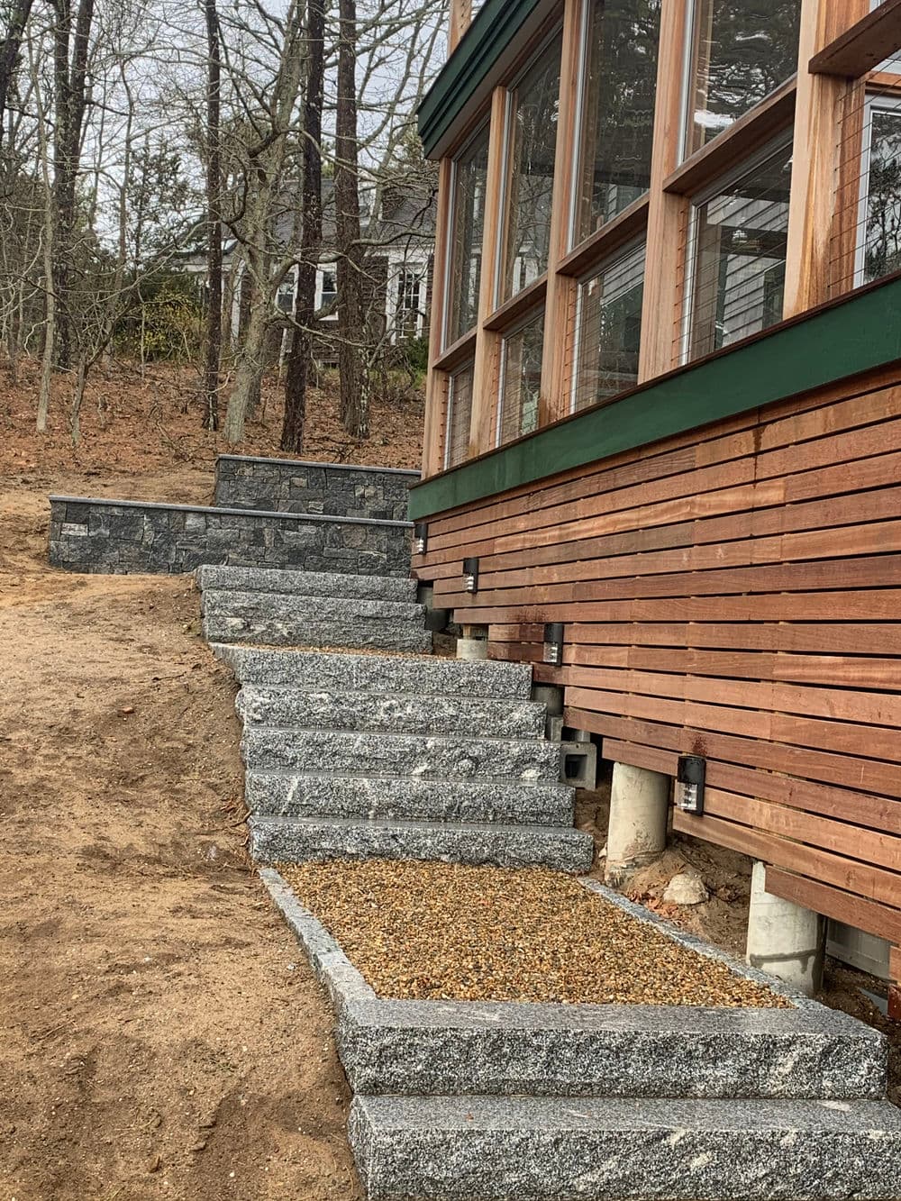 Stone steps leading to a wooden house with large windows and a natural landscape backdrop.