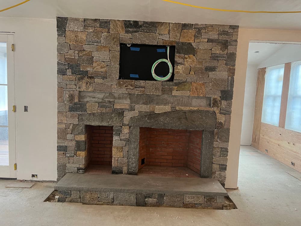 Stone fireplace with two openings and mounted TV area, set in an unfinished room.