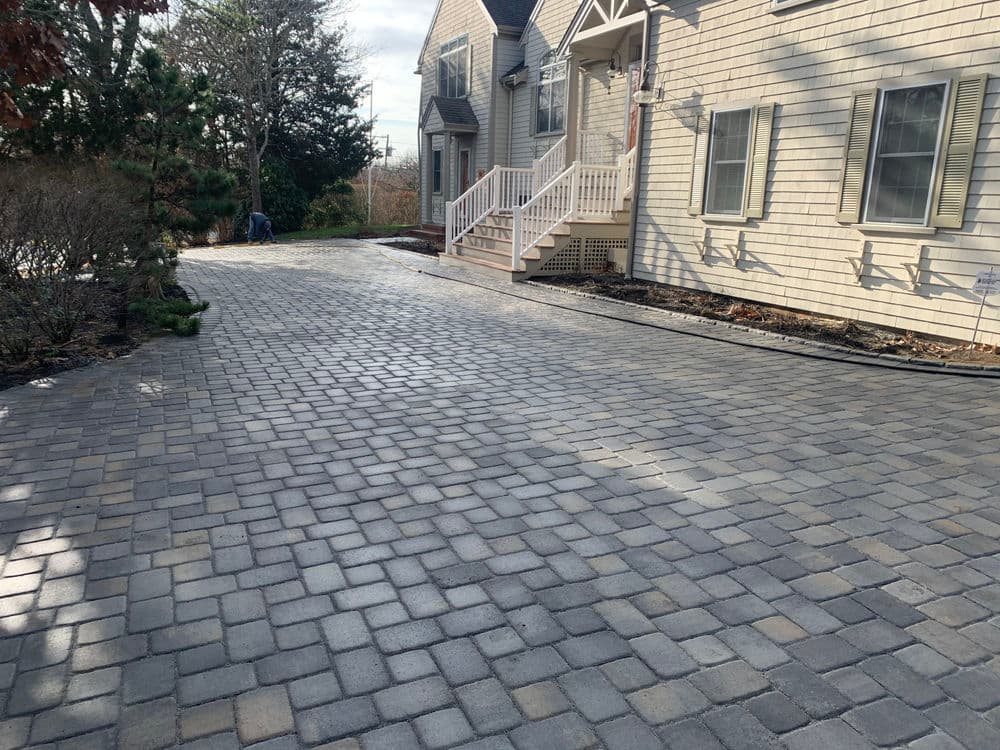 Paved driveway with gray cobblestones leading to a house and landscaped areas.