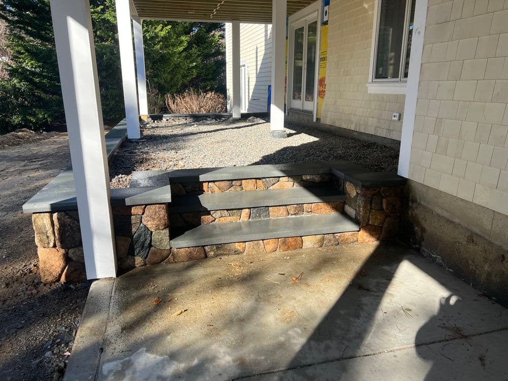 Stone steps leading to a covered porch, surrounded by gravel and greenery.