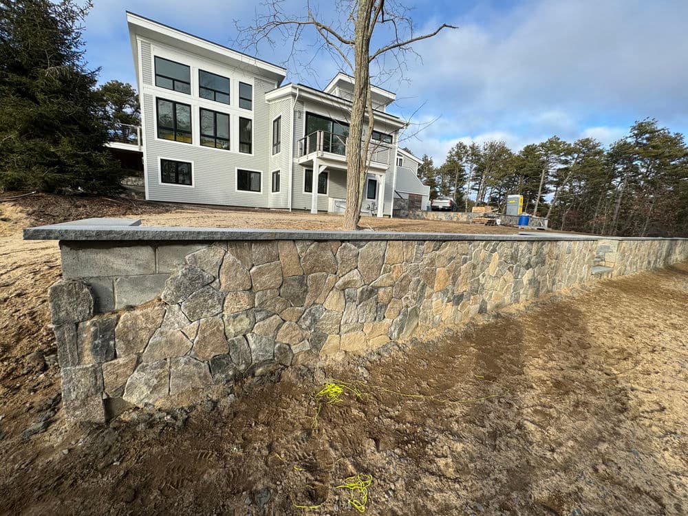 Modern home with large windows and stone retaining wall in a landscaped yard.