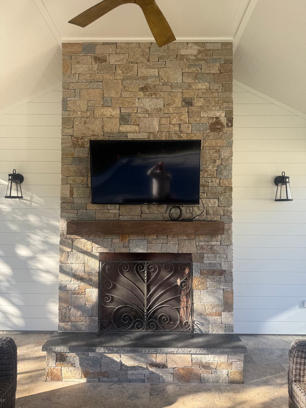 Modern stone fireplace with TV, stylish wall sconces, and elegant fan in a cozy living space.