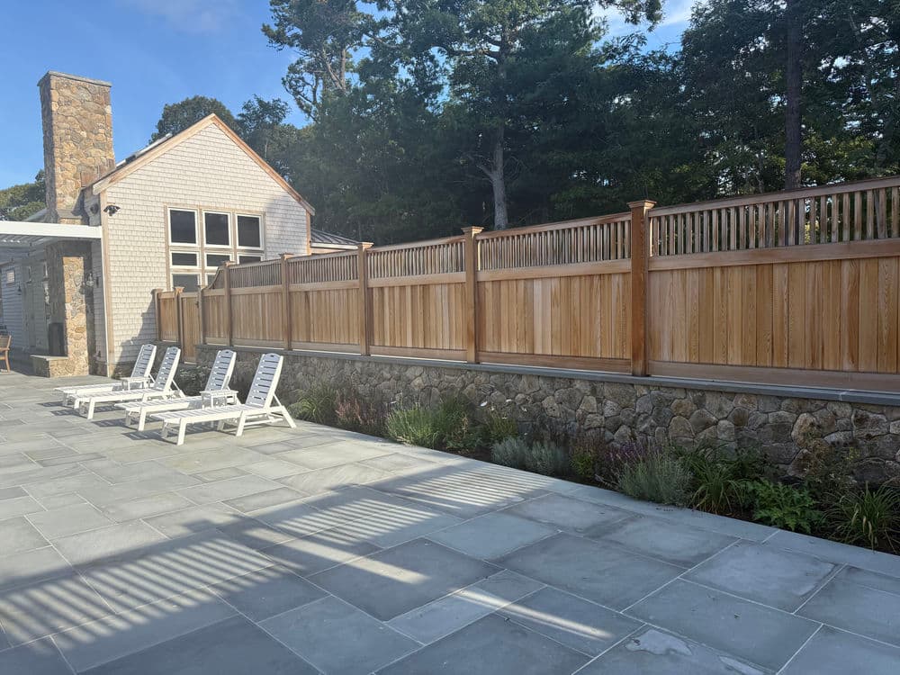 Modern outdoor space with lounge chairs, wooden fence, and landscaped garden by a home.
