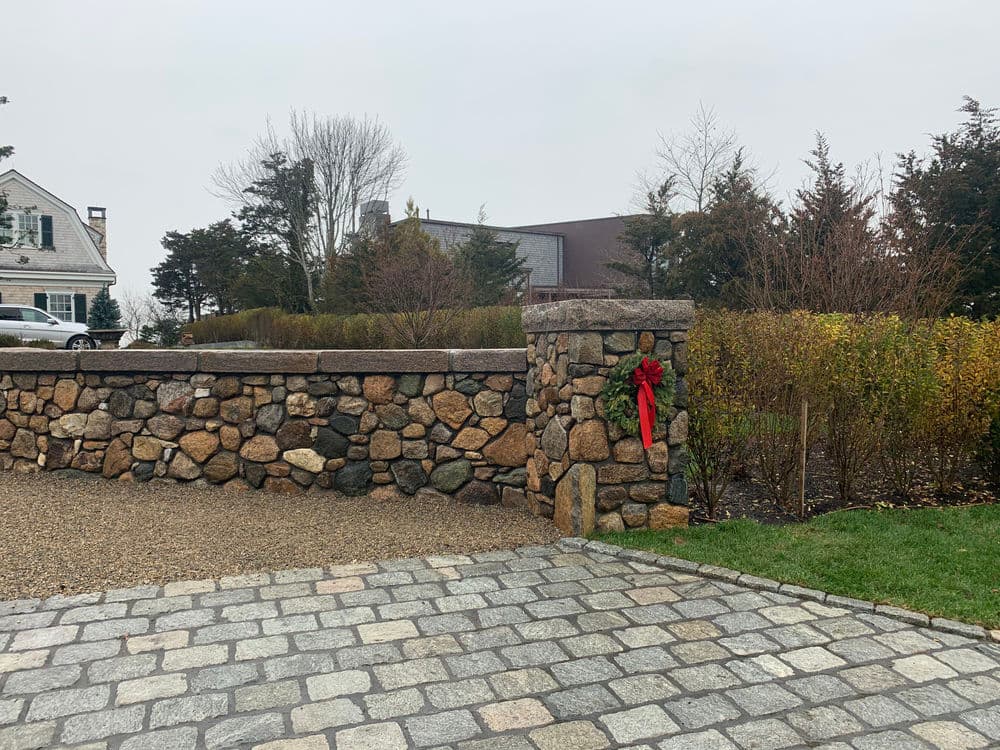 Stone wall with a red wreath, surrounded by landscaped greenery and gravel pathway.