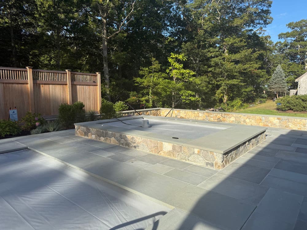 Modern outdoor patio with stone features and landscaping surrounded by trees.