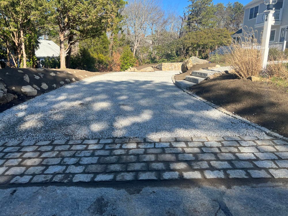 Newly constructed gravel driveway with cobblestone border and landscaped surroundings.