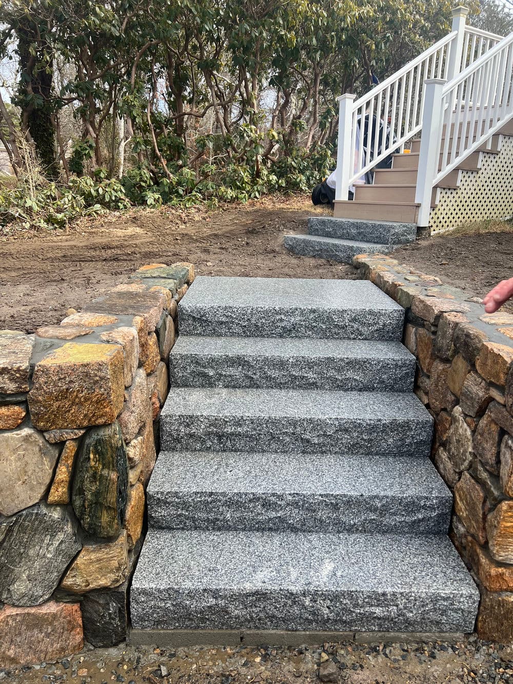 Granite stone steps leading to a home, surrounded by natural landscaping and stone wall.
