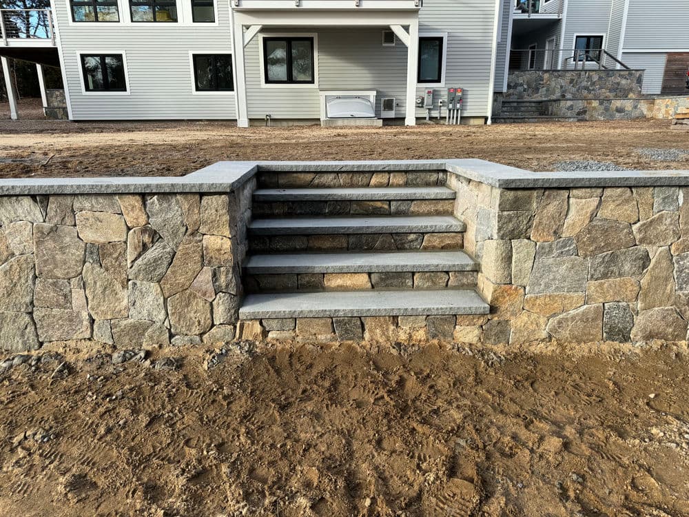 Stone steps leading to a modern home with stone walls and a gravel yard.