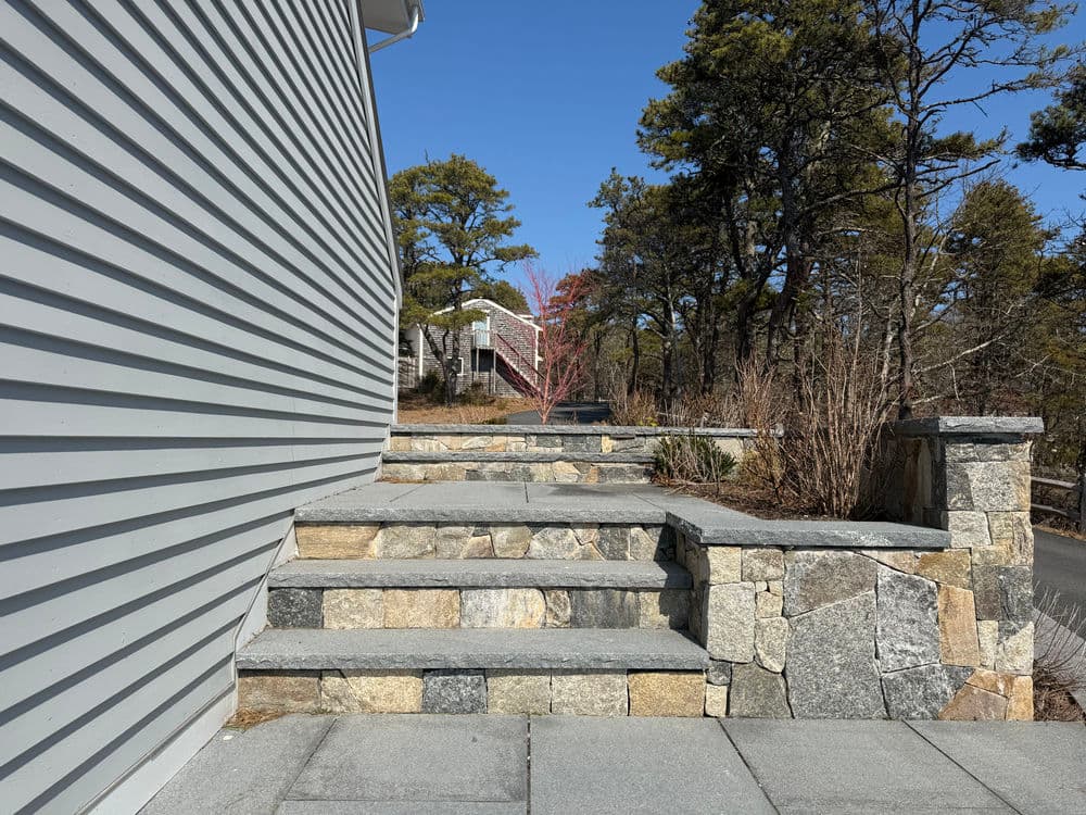 Stone steps leading up to a modern home with landscaped surrounding and trees.